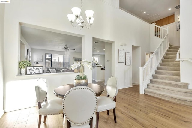 dining area featuring a towering ceiling, ceiling fan with notable chandelier, and light wood-type flooring