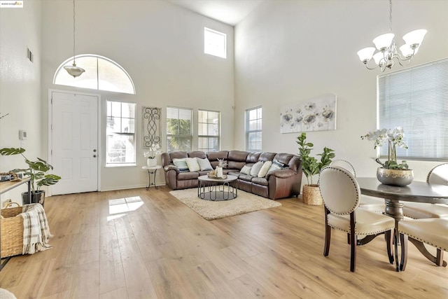 living room with a towering ceiling, a chandelier, a healthy amount of sunlight, and light wood-type flooring