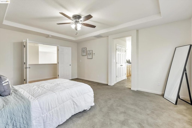 carpeted bedroom featuring ceiling fan, a tray ceiling, and ensuite bath