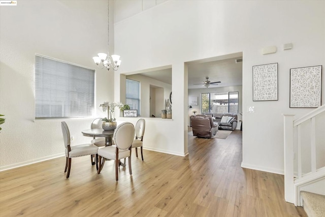 dining area with a high ceiling, ceiling fan with notable chandelier, and light hardwood / wood-style floors