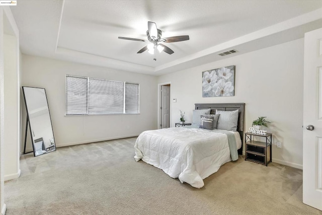 bedroom with ceiling fan, a tray ceiling, and light carpet