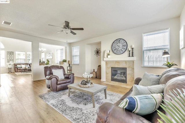 living room featuring ceiling fan with notable chandelier, a fireplace, a healthy amount of sunlight, and light wood-type flooring