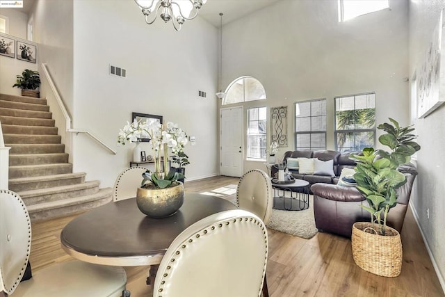 dining area with a high ceiling, a notable chandelier, and light hardwood / wood-style flooring