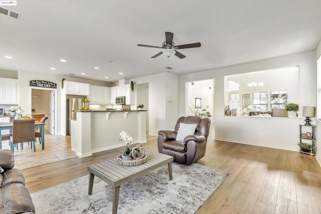 living room with ceiling fan with notable chandelier and light hardwood / wood-style floors