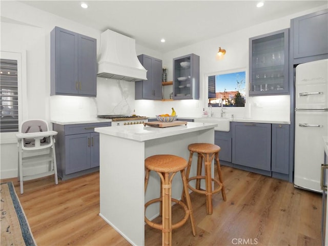 kitchen featuring sink, a breakfast bar area, refrigerator, a kitchen island, and custom range hood