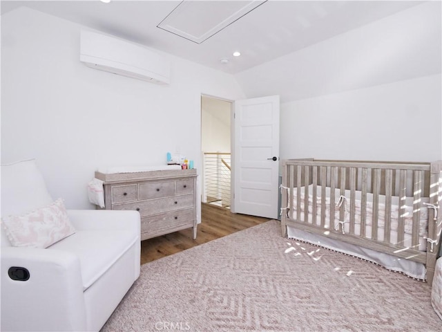 bedroom featuring dark hardwood / wood-style flooring, vaulted ceiling, an AC wall unit, and a nursery area