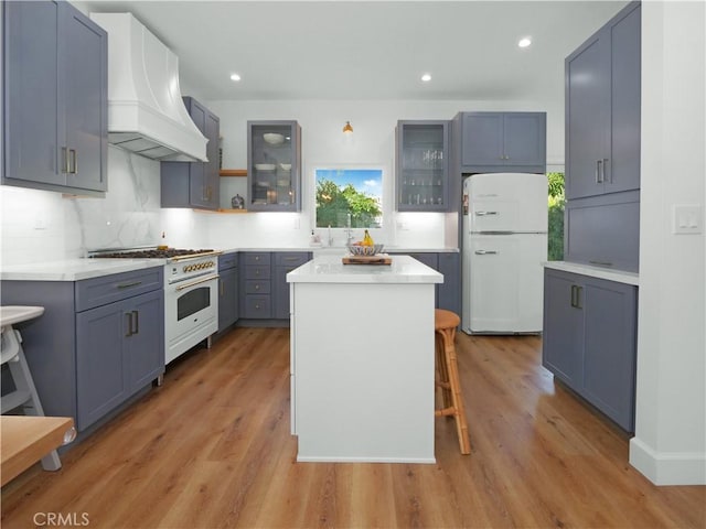 kitchen featuring a kitchen bar, light hardwood / wood-style flooring, custom range hood, a kitchen island, and white appliances