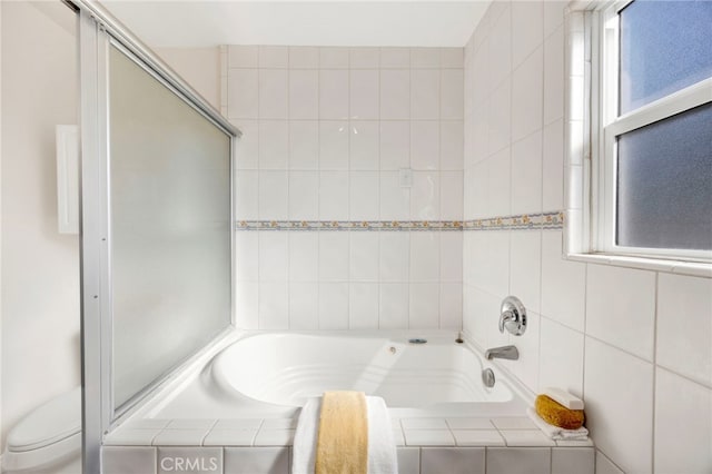 bathroom with a relaxing tiled tub, toilet, and a wealth of natural light