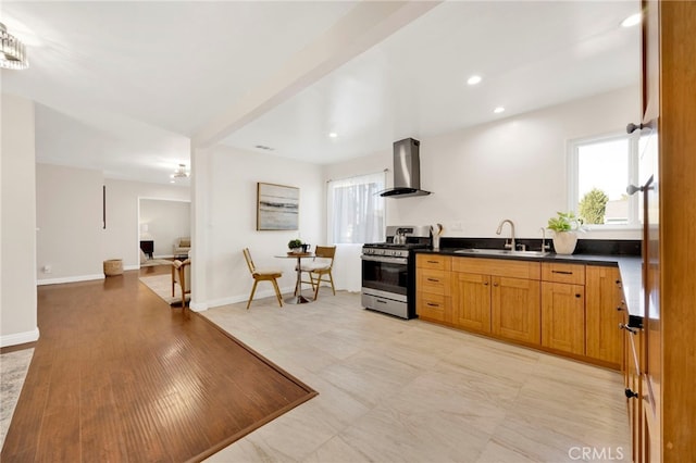 kitchen featuring stainless steel gas range oven, sink, wall chimney range hood, and a wealth of natural light