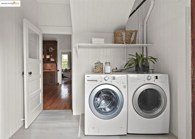 laundry room featuring light wood-type flooring, independent washer and dryer, and wood walls