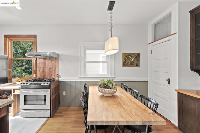 kitchen with wood walls, decorative light fixtures, dark brown cabinetry, stainless steel range with gas stovetop, and light wood-type flooring