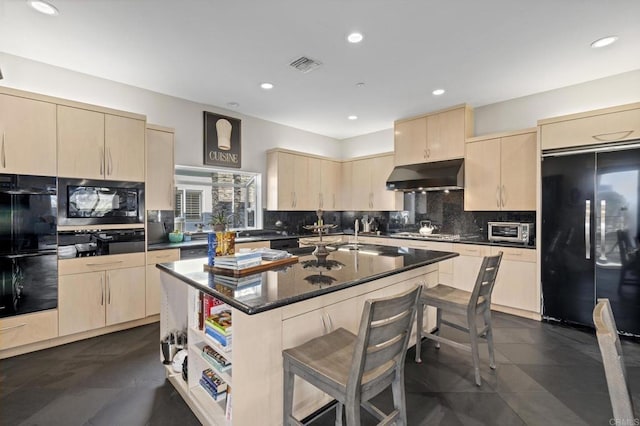 kitchen featuring black appliances, a kitchen island with sink, light brown cabinets, and exhaust hood