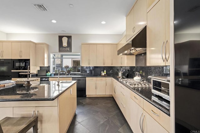 kitchen with dark stone countertops, light brown cabinets, wall chimney range hood, decorative backsplash, and black appliances