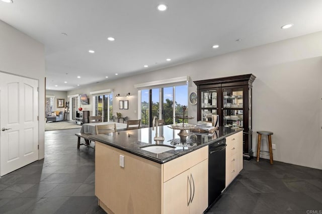 kitchen featuring an island with sink, sink, light brown cabinets, and dark stone countertops