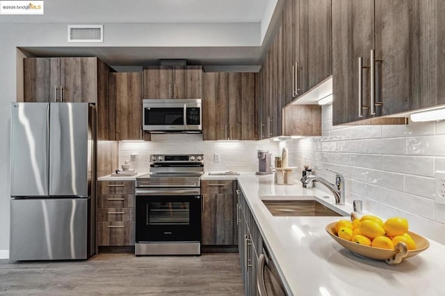 kitchen featuring sink, backsplash, light hardwood / wood-style floors, and appliances with stainless steel finishes