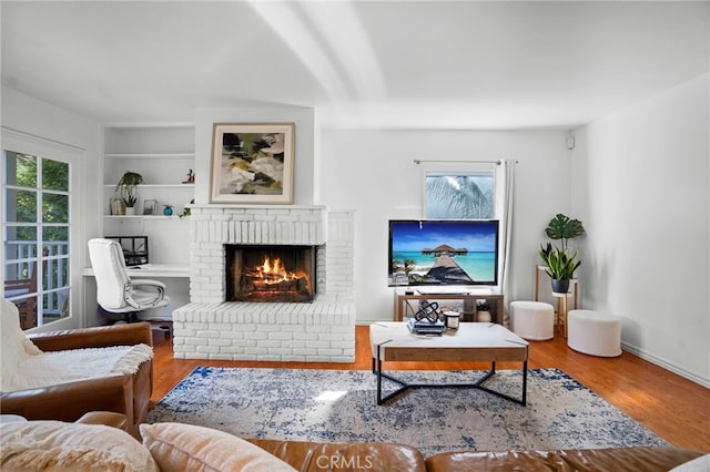 living room with wood-type flooring, a brick fireplace, and built in features