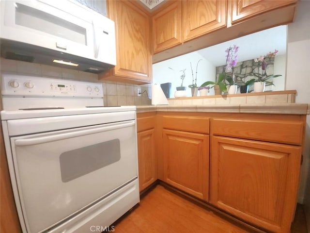 kitchen featuring white appliances, tile counters, light hardwood / wood-style floors, and decorative backsplash