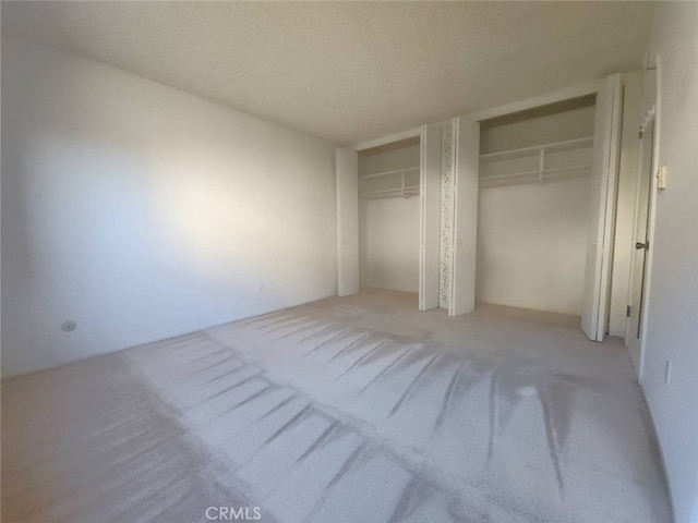 unfurnished bedroom with light carpet, two closets, and a textured ceiling