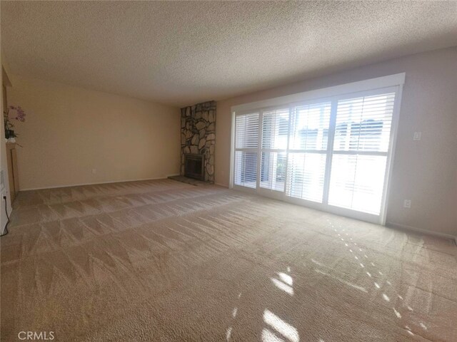 unfurnished living room with a stone fireplace, carpet floors, and a textured ceiling