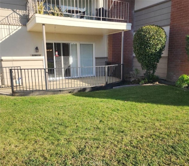 view of exterior entry featuring a balcony and a lawn