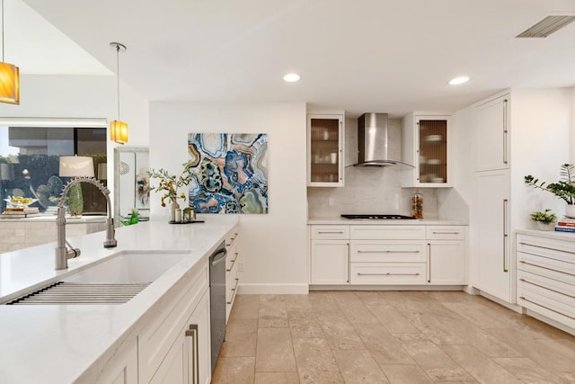 kitchen with dishwasher, sink, white cabinets, hanging light fixtures, and wall chimney range hood