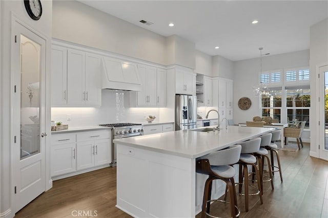 kitchen featuring a kitchen island with sink, decorative light fixtures, stainless steel appliances, and white cabinets