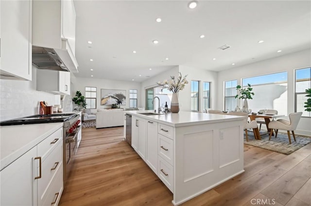 kitchen featuring sink, custom exhaust hood, light hardwood / wood-style flooring, a kitchen island with sink, and white cabinets