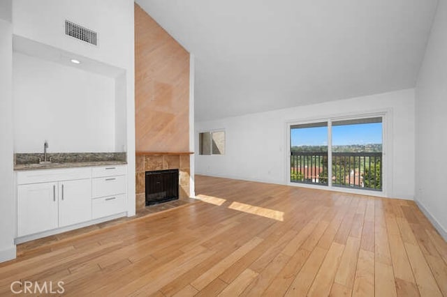 unfurnished living room featuring a tiled fireplace, high vaulted ceiling, sink, and light hardwood / wood-style floors