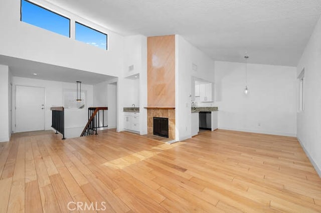 unfurnished living room with a tiled fireplace, light wood-type flooring, and a high ceiling