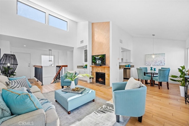 living room with high vaulted ceiling, a tiled fireplace, wood finished floors, and visible vents