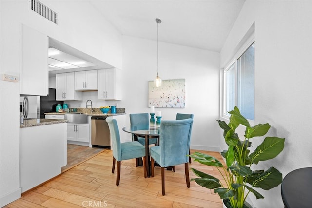 dining space featuring light wood-type flooring, visible vents, lofted ceiling, and baseboards