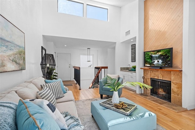 living area featuring a towering ceiling, light wood-style floors, visible vents, and a tile fireplace