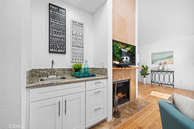 bar with a tile fireplace, a sink, light wood-style flooring, and wet bar