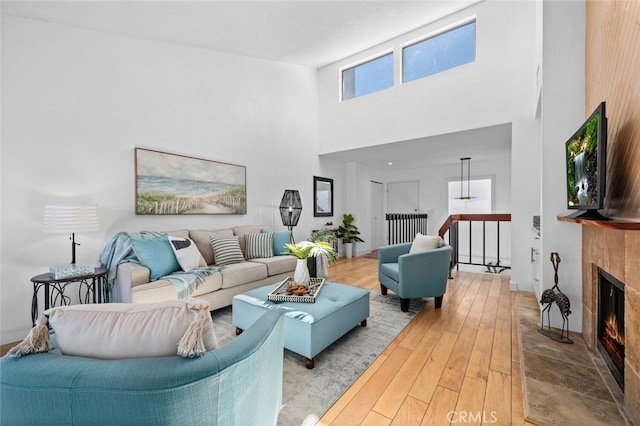 living area with a towering ceiling, light wood finished floors, and a lit fireplace