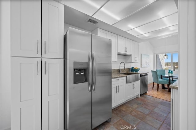 kitchen with light stone counters, stainless steel appliances, visible vents, white cabinetry, and a sink