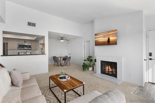 living room with a high ceiling, ceiling fan, light carpet, and a fireplace