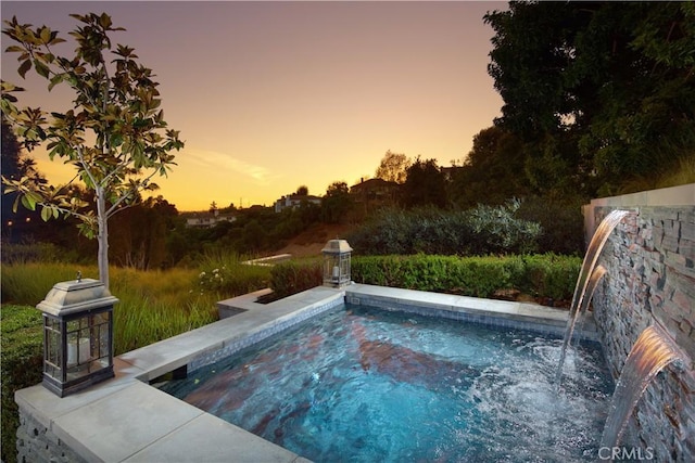 pool at dusk featuring pool water feature