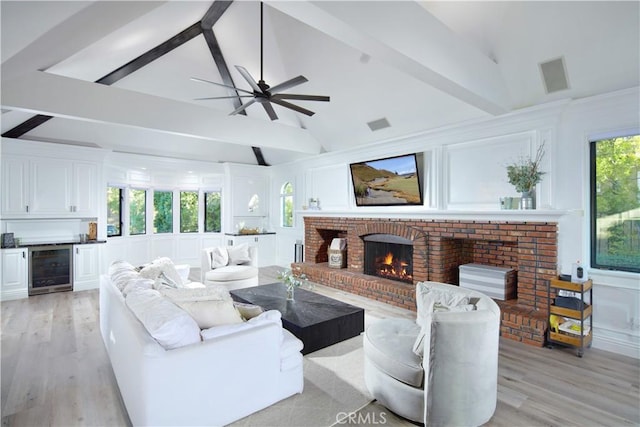 living room with wine cooler, a fireplace, lofted ceiling with beams, and light hardwood / wood-style flooring