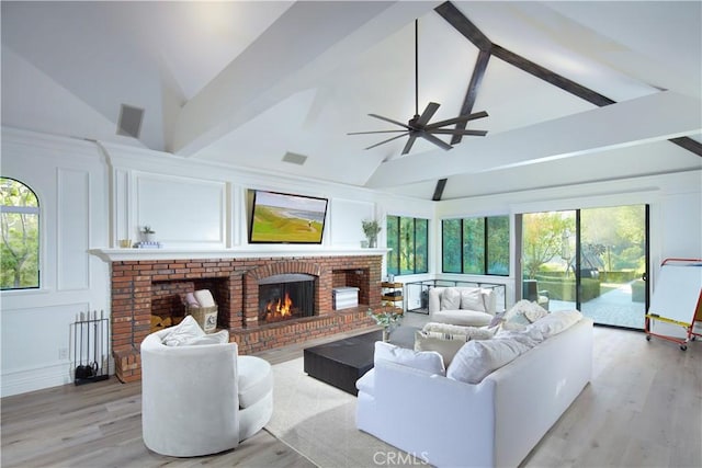 living room with ceiling fan, beam ceiling, light hardwood / wood-style floors, and a brick fireplace