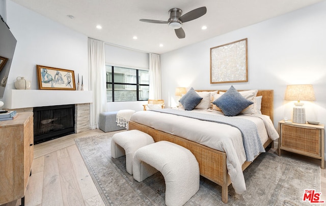 bedroom featuring ceiling fan, a fireplace, and light wood-type flooring