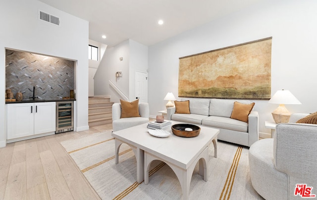 living room with a high ceiling, indoor wet bar, beverage cooler, and light wood-type flooring