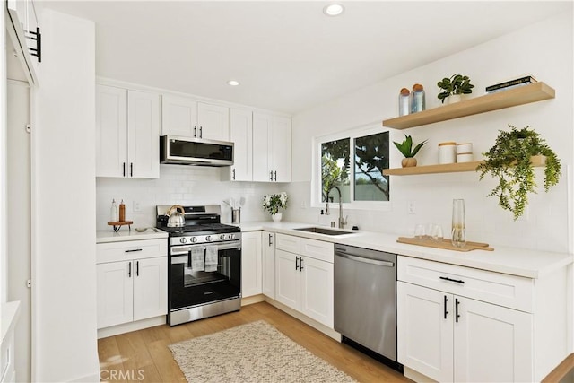 kitchen featuring sink, white cabinets, backsplash, stainless steel appliances, and light hardwood / wood-style flooring