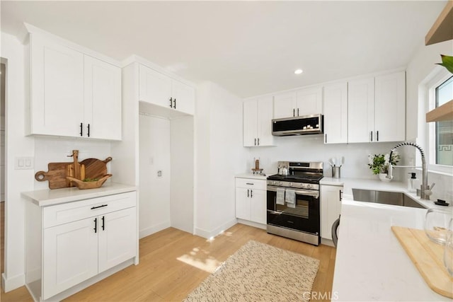 kitchen with light wood-type flooring, stainless steel appliances, sink, and white cabinets