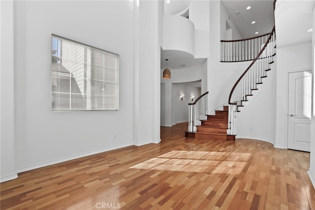 entrance foyer featuring stairway, light wood-style flooring, baseboards, and a high ceiling