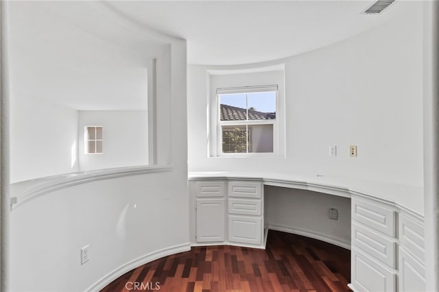 unfurnished office featuring dark wood finished floors, built in desk, and visible vents