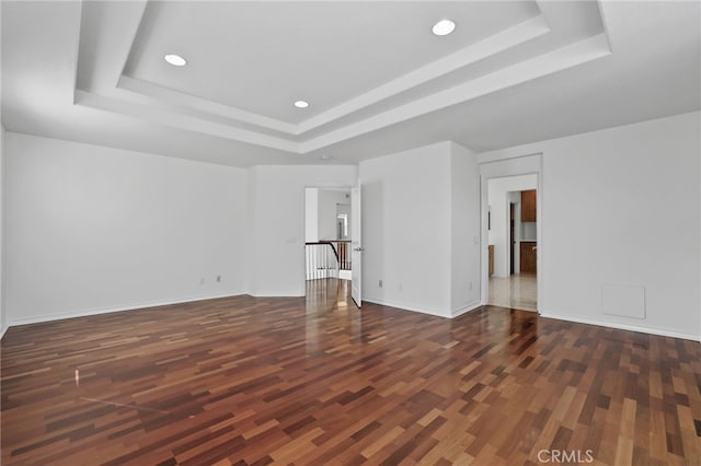 spare room with a tray ceiling, recessed lighting, wood finished floors, and baseboards