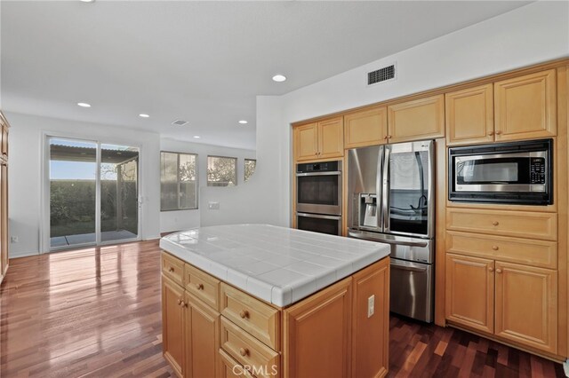 kitchen featuring dark hardwood / wood-style floors, appliances with stainless steel finishes, tile counters, and a kitchen island