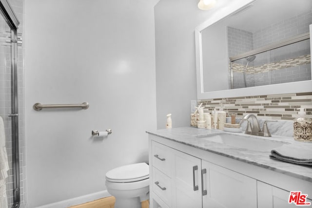 bathroom with tasteful backsplash, vanity, a shower with shower door, and toilet