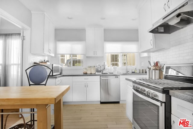 kitchen featuring white cabinetry, tasteful backsplash, stainless steel appliances, and dark stone counters