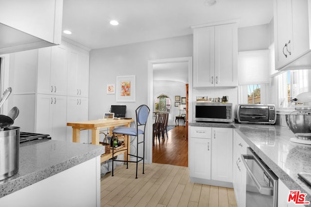 kitchen with stainless steel appliances, white cabinets, light wood-type flooring, and decorative backsplash